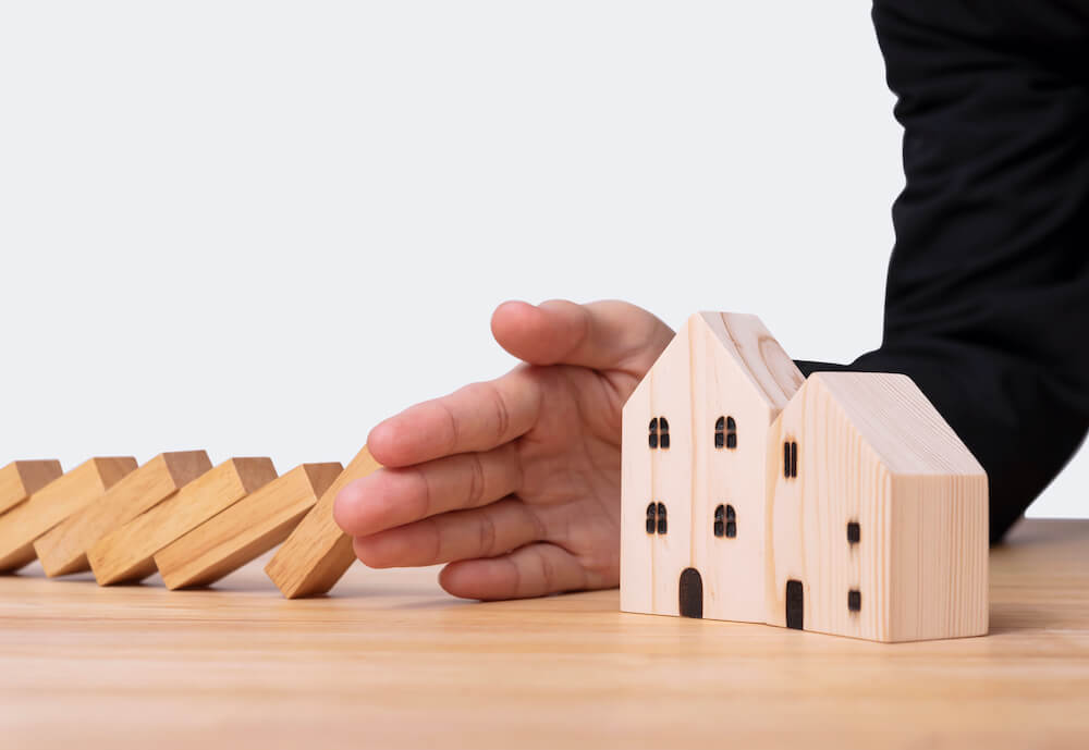 Hand zwischen fallenden Domino-Steinen und Bauklotzhaus